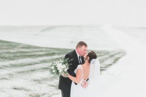 bride and groom kissing outside in snowy field